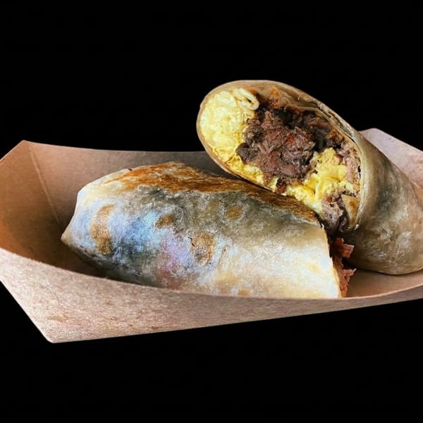 Two Muchachos breakfast burritos, one cut open to show scrambled eggs and shredded beef.
