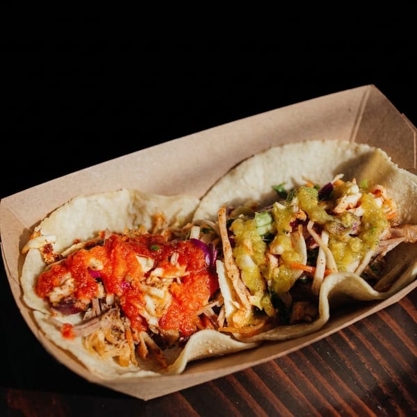 Two Muchachos tacos, one with red salsa and one with green salsa, in a cardboard tray.