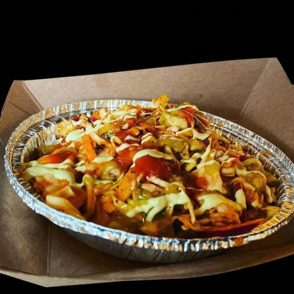 Muchachos' Mexican nachos in a foil container, topped with red and white sauces, and vegetables.