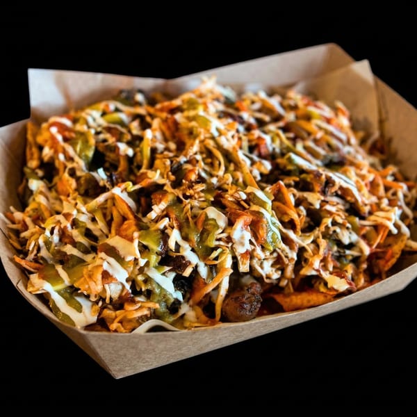 Muchachos' Mexican nachos in a cardboard tray, topped with green and white sauces, and shredded vegetables.