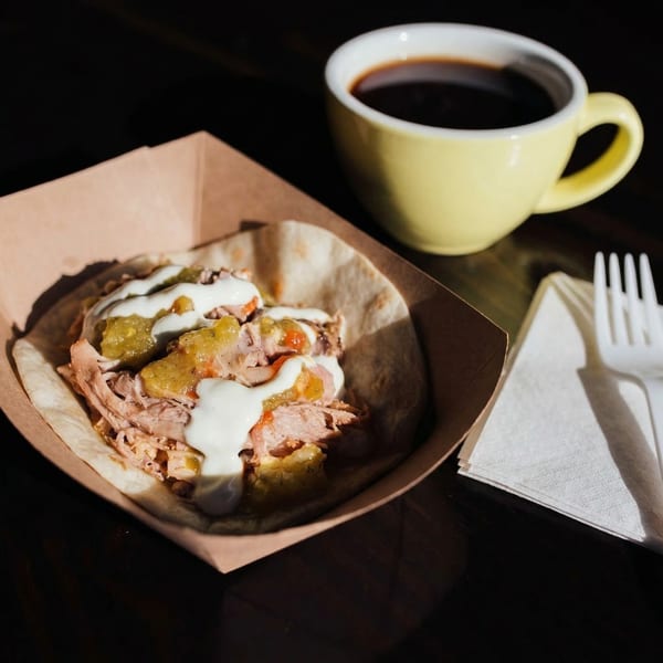 Muchachos' carnitas taco with salsa verde and crema, alongside a cup of coffee.