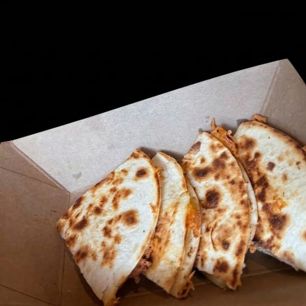 Four quesadilla wedges with browned tortillas and melted cheese, served in a brown takeout box.